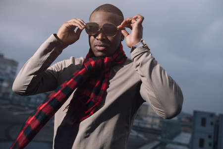 Brutal african american man with scarf and sunglasses in city sky backgroundの写真素材