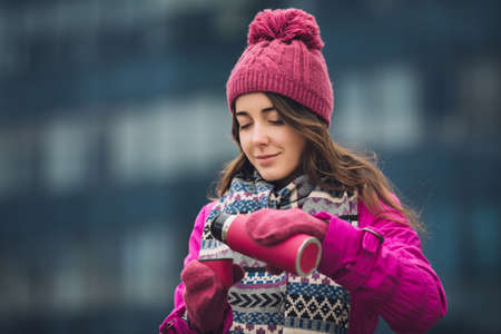 Woman in bright winter jacket pouring tea into thermos outdoorの写真素材