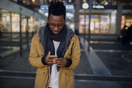 African man using smartphone at night standing in dark city, he type sms message