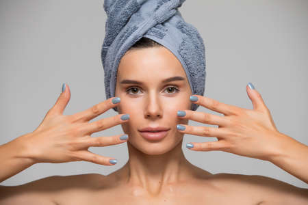 Beautiful spa woman isolated on grey background. She after bath with towel on head. Hands near face.の写真素材