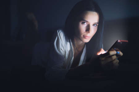 Woman using blue screen of smartphone at night, online dating serviceの写真素材