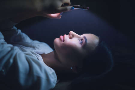 Woman using blue screen of smartphone at night before sleep