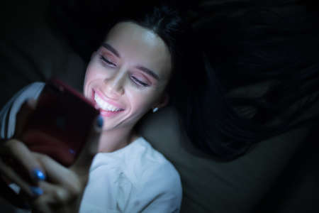 Woman using blue screen of smartphone at night before sleepの写真素材
