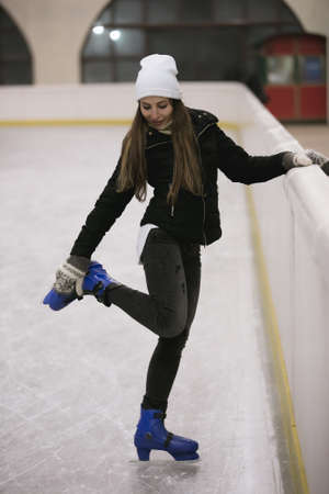 Young woman standing on ice of a skating rink fastens her skatesの写真素材