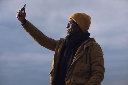 African man in hat and jacket make selfie photo over sky backgroundの写真素材