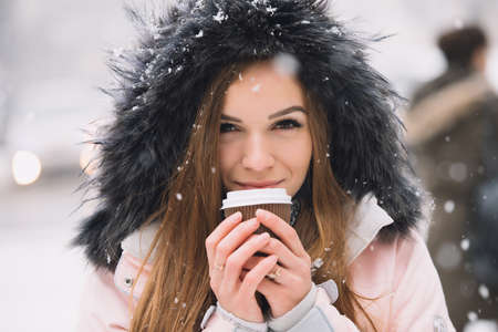 Beautiful young woman holding paper coffee cup at winter urban city