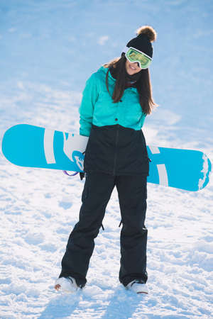 Leisure, winter, sport concept - happy young woman snowboarder standing with boardの写真素材