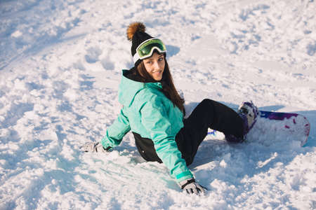 Smiling girl snowboarder sit on a snowの写真素材