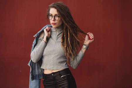 Stylish woman with dreadlocks posing against red wall background