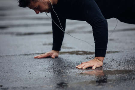 Young athletic man push ups in the rain