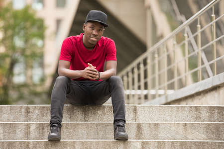 Stylish man in pink t-shirt sitting in urban city streetの写真素材