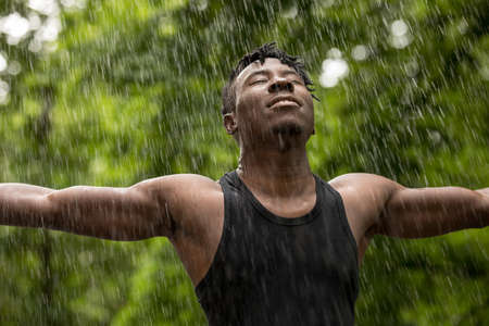 African man enjoying fresh summer rain while hands raisedの写真素材