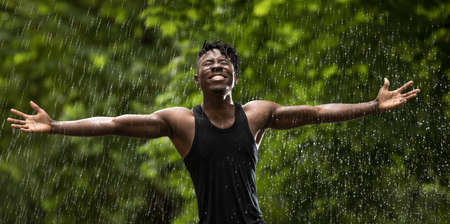 African man enjoying fresh summer rain while hands raised