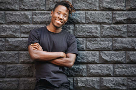Handsome smiling african american man in blank black t-shirt standing against brick wall