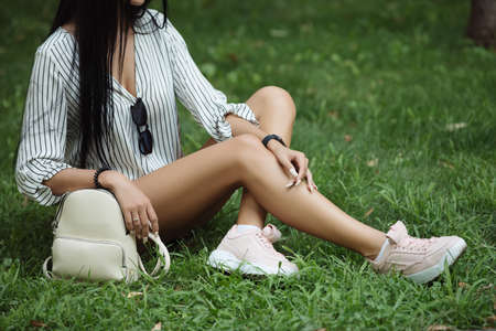 Female legs sitting on grass, bag near herの写真素材