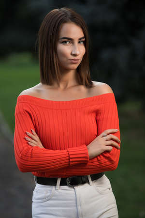 Portrait of confident strict woman in red sweater at the autumn park with arms crossed