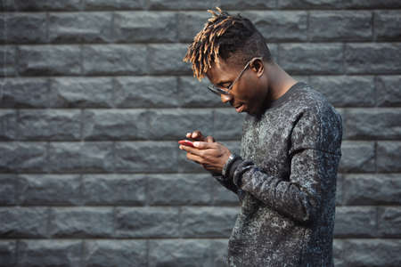 African american man using mobile phone app at brick wall background