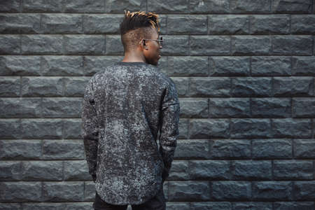 Fashionable man in pullover standing against brick wall background, back viewの写真素材