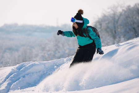 Woman snowboarder riding down from snowy hillの写真素材