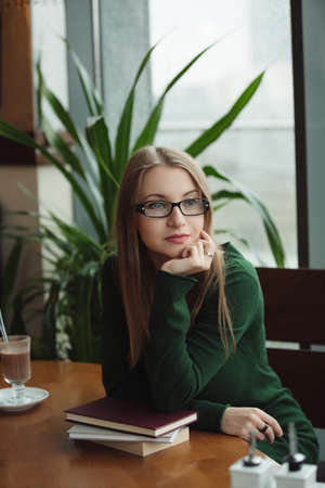 Portrait of intelligent woman sitting with books in cafe