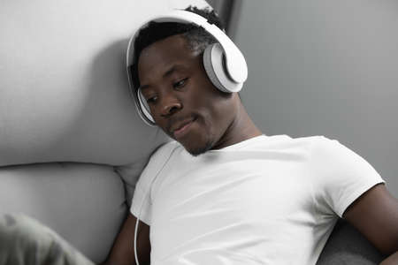 African man listening to music at home in headphonesの写真素材