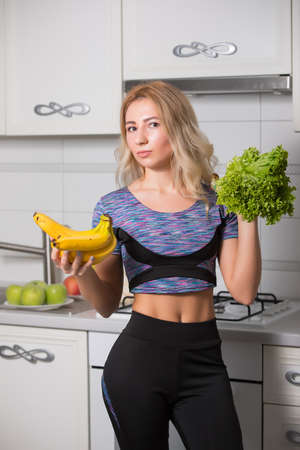 Portrait of woman holding bananas and salad on kitchen, healthy food conceptの写真素材
