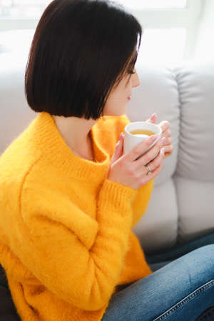 Woman drinking tea cup in apartment sitting on sova at the morning weekend rest day