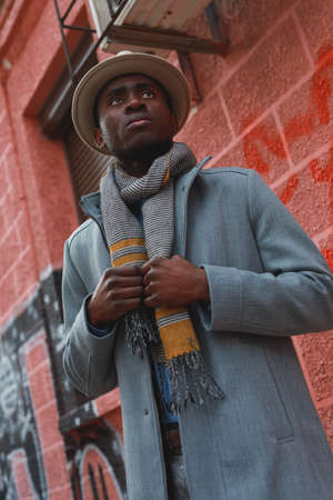 Street portrait of african american man in coat and hat at the red building background