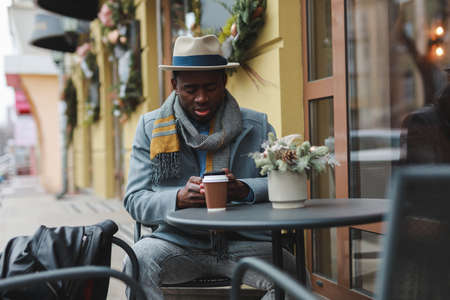 African american man using smartphone sitting at outdoor cafeの写真素材