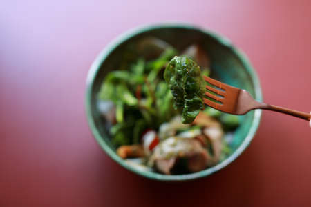 Eating healthy fresh salad with fork on a light marsala color table