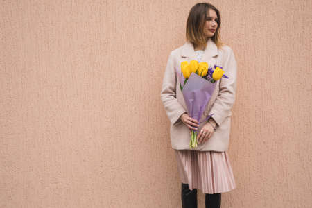 Woman holding a bouquet of yellow tulips at the beige wall