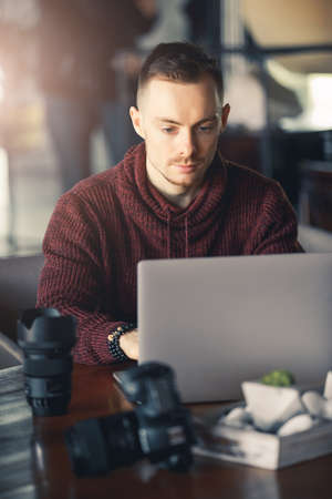 Man photographer or videomaker retouches photos or edits video project using laptop in a cafeの写真素材