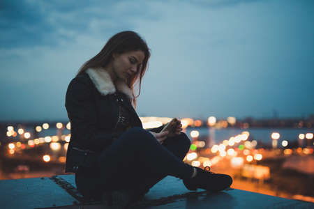 Silhouette of alone woman sitting on the roof, evening sky background, city scapeの写真素材