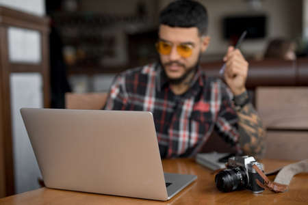 Stylish handsome man in checkered shirt blogger or freelancer looks at the laptop computer monitor in cafeの写真素材
