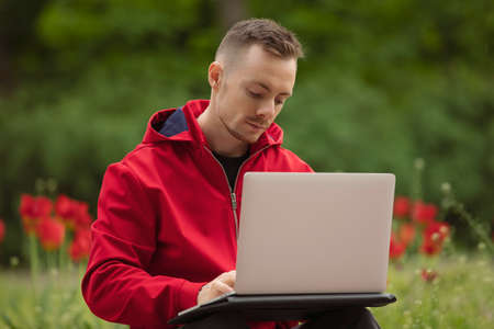 Man freelancer blogger in red jacket working by laptop computer at the summer parkの写真素材
