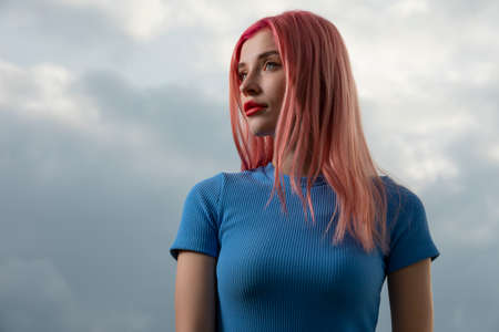 Unconventional beautiful woman with pink hair against sky background, creative art portraitの写真素材