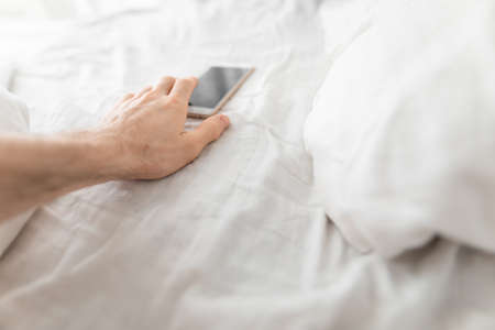 1st person view, male hand reaches for the smartphone immediately after waking up in bedの写真素材