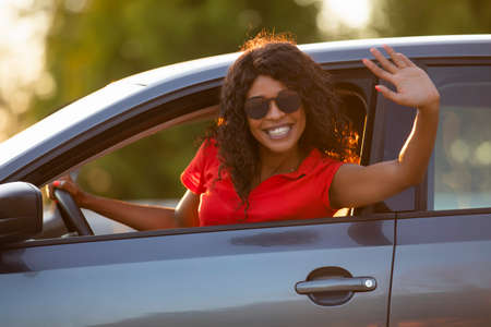 Happy woman driver sitting in car salon and waving handの写真素材