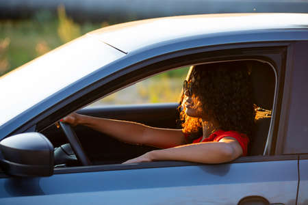 Happy woman driver sitting in car salon at gold sunsetの写真素材