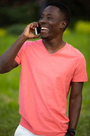African american man in living coral t-shirt talking by smartphone at summer dayの写真素材
