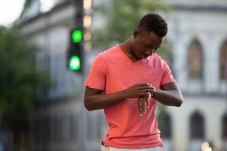 African american man in living coral t-shirt looks time at handle watch in cityの写真素材