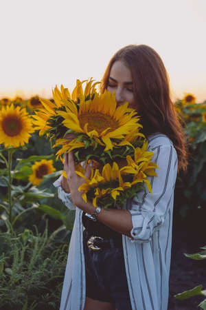 Beautiful woman sniff a flower in sunflower fieldの写真素材