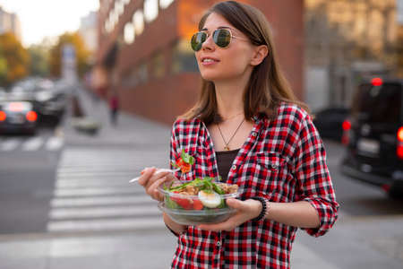Young woman eating salad at urban city outdoor, fast dinner snack