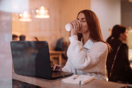 Woman working by laptop in cafe, view through window