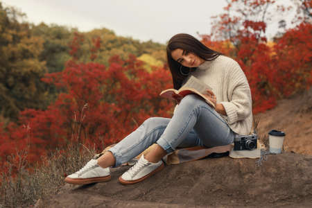 Woman reading book sitting in the nature drinking tea, colorful autumn aroundの写真素材
