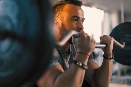 Man lifting barbell in a gym on EZ bar preacher curl, making biceps exercise