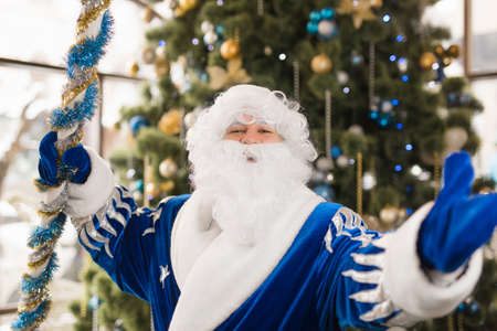 Blue Santa celebrating New Year holiday against Christmas treeの写真素材