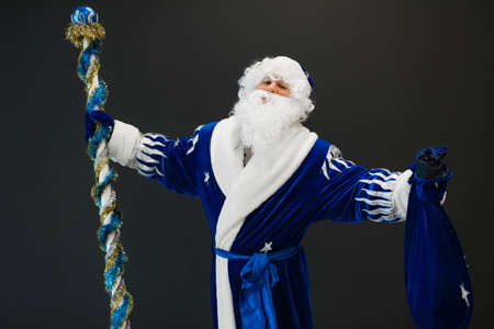 Happy blue Santa portrait celebrating Christmas holiday on black background with raised handsの写真素材
