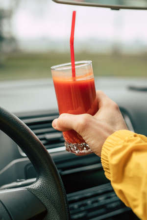 Man driver holding glass with tomato juice in a car