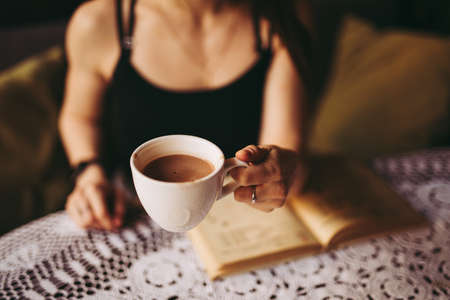 Woman holding cup with hot chocolate while reading book in cafeの写真素材